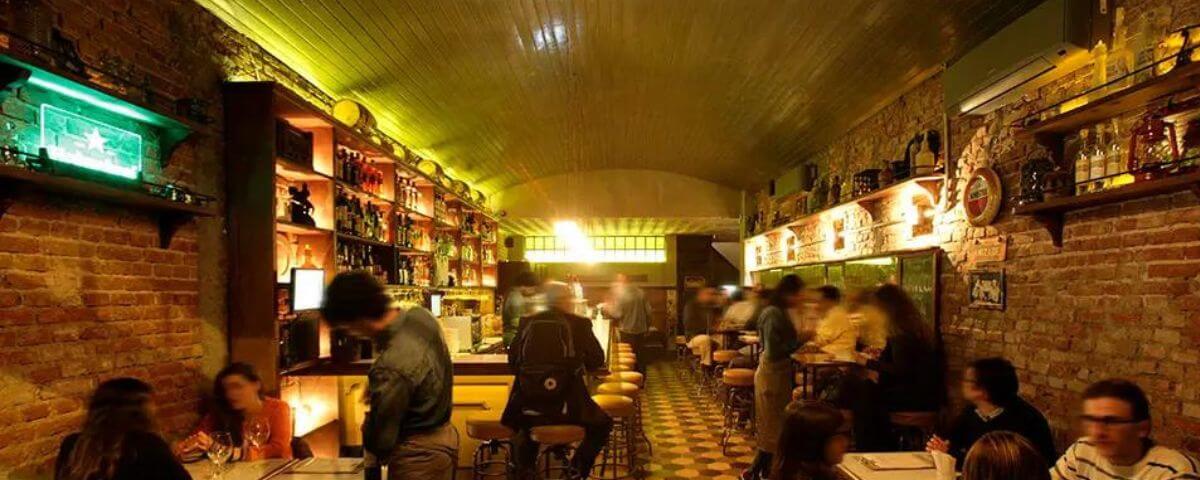 O salão do Sóshots & Gin Club, um dos bares no Itaim Bibi, tem o teto arredondado, com luzes amarelas nas laterais, mesas espalhadas pelo salão e banquetas para quem quiser sentar no bar. 