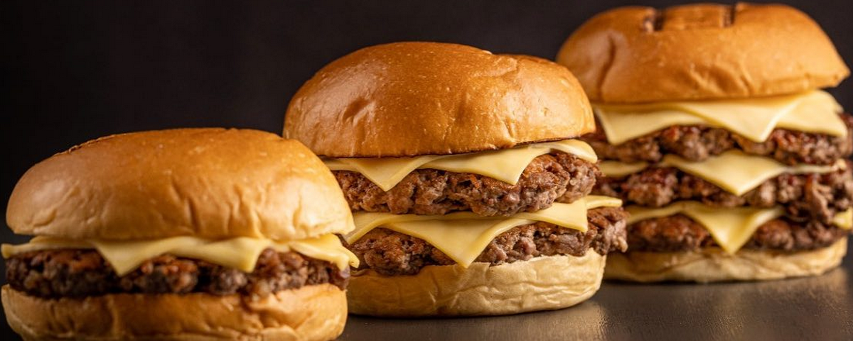 Três hambúrguers são servidos no Bullger. O primeiro tem um hambúrguer de carne dentro, o segundo dois e terceiro três, da esquerda para a direita. Todos possuem pão e queijo também. 