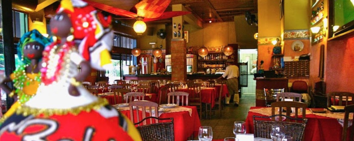 O restaurante Consulado da Bahia também serve comida baiana em SP. Ele tem diversas mesas espalhadas com toalhas vermelhas e uma decoração colorida. 