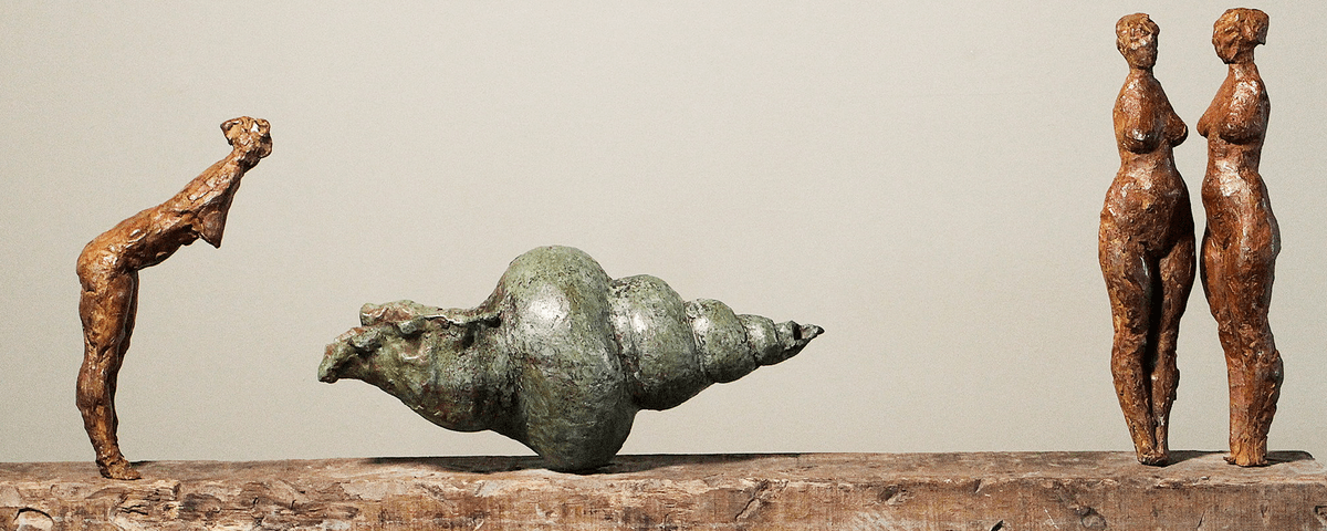 Esculturas feitas em metal, onde do lado esquerdo um corpo feminino se curva, no centro uma escultura em formato de concha e mais dos corpos femininos, lado a lado, na parte direita. 