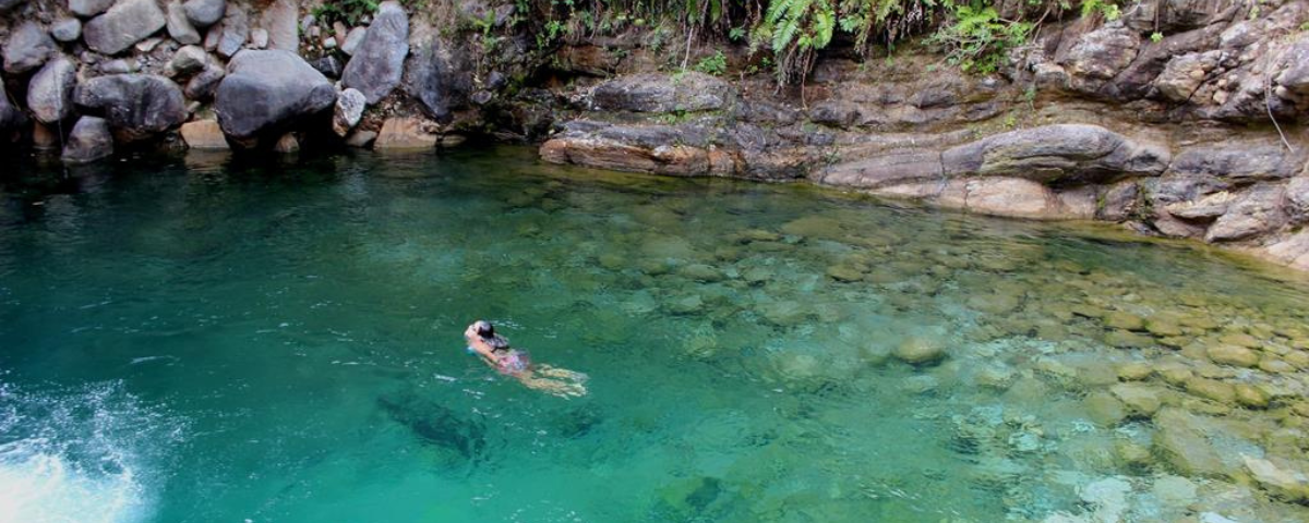 Mulher mergulha nas águas azuis turquesa do Poço Azul. Ao redor há várias pedras e essa é mais uma das belas piscinas naturais de SP. 