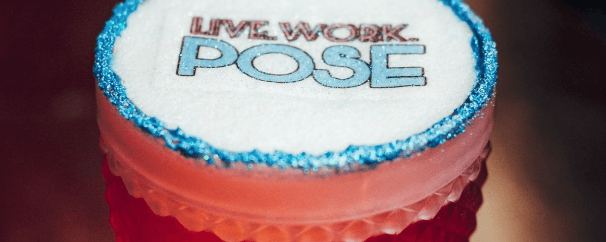 Drink cor de rosa, com glitter azul na borda do copo, tem escrito "Live, Work, Pose". O Bar Spoiler é um dos bares diferentes de SP e tem diversas bebidas temáticas. 