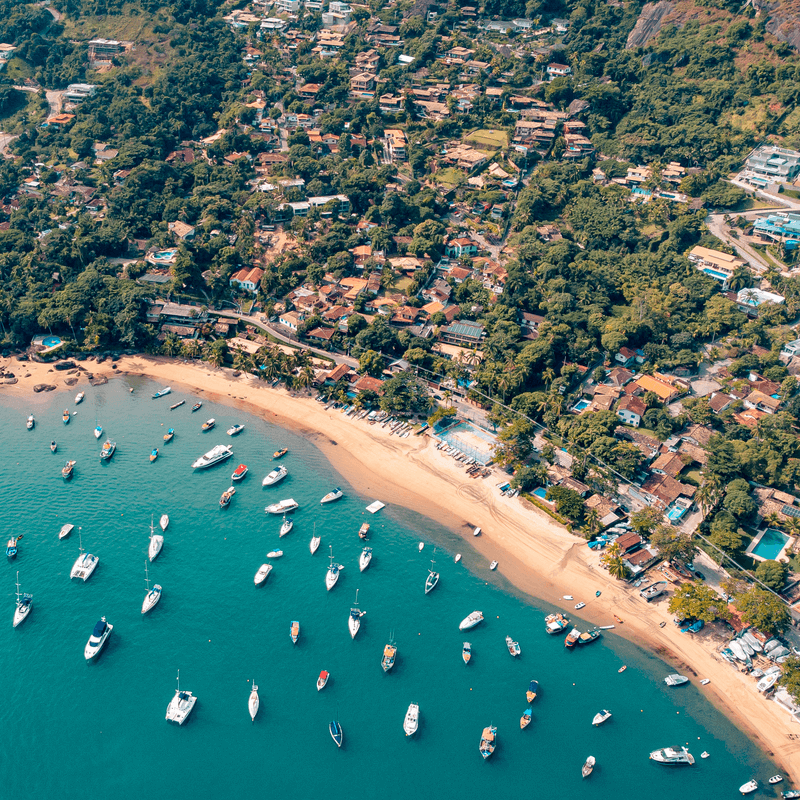 Vista aérea de Ilhabela, com diversos barcos no mar, além de casas e árvores perto da praia. 