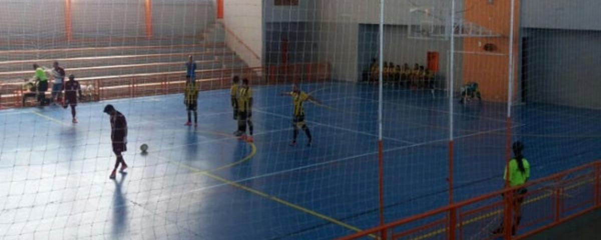 Alunos jogam futsal em uma quadra esportiva. 