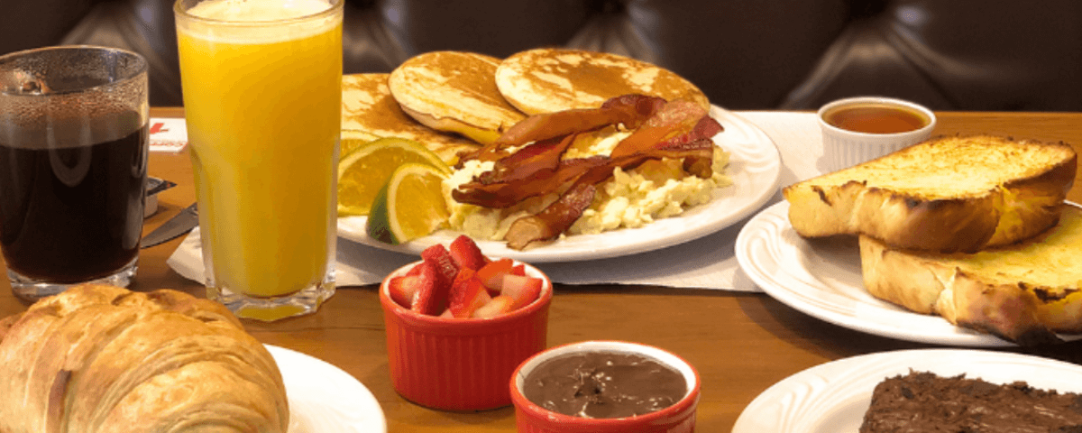 Um café da manhã típico da gastronomia americana, com panqueca, ovos, bacon e  torradas. 