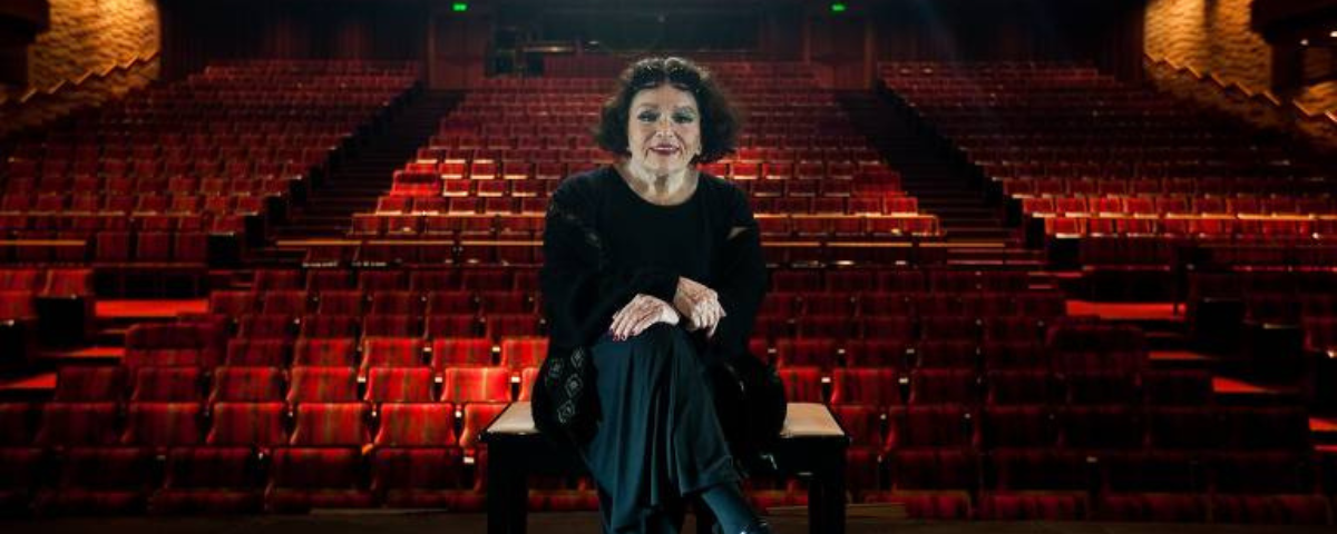 Atriz Bibi Ferreira sentada no palco do teatro que leva o seu nome. 