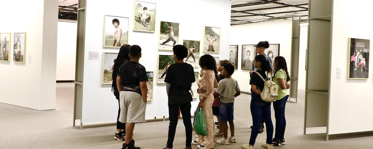 Grupo de adolescentes observa quadros expostos em museu. 