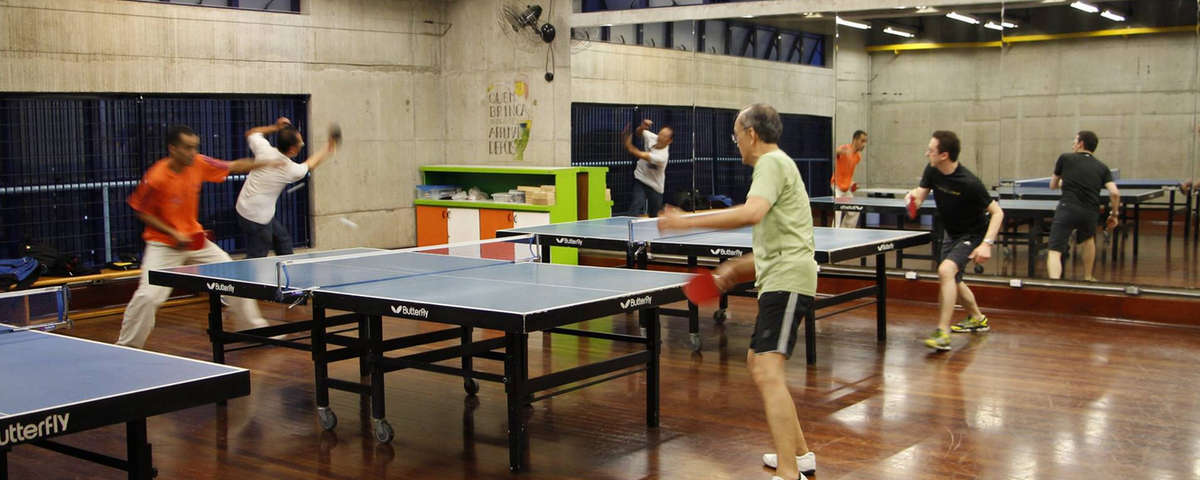 Sala com diversas pessoas praticando tênis de mesa em SP. 