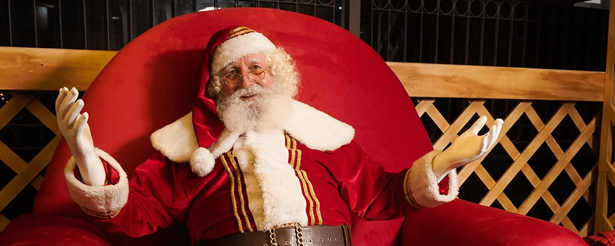 Homem fantasiado de Papai Noel, sentado em uma poltrona vermelha. 