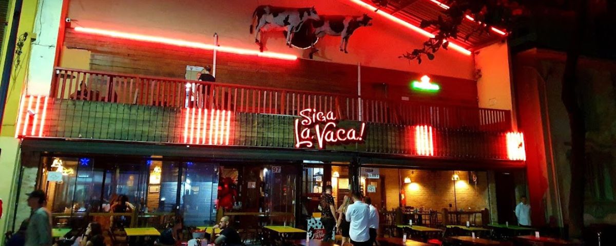 Fachada do Siga La Vaca, um karaokê em SP, possui um letreiro vermelho iluminado. 