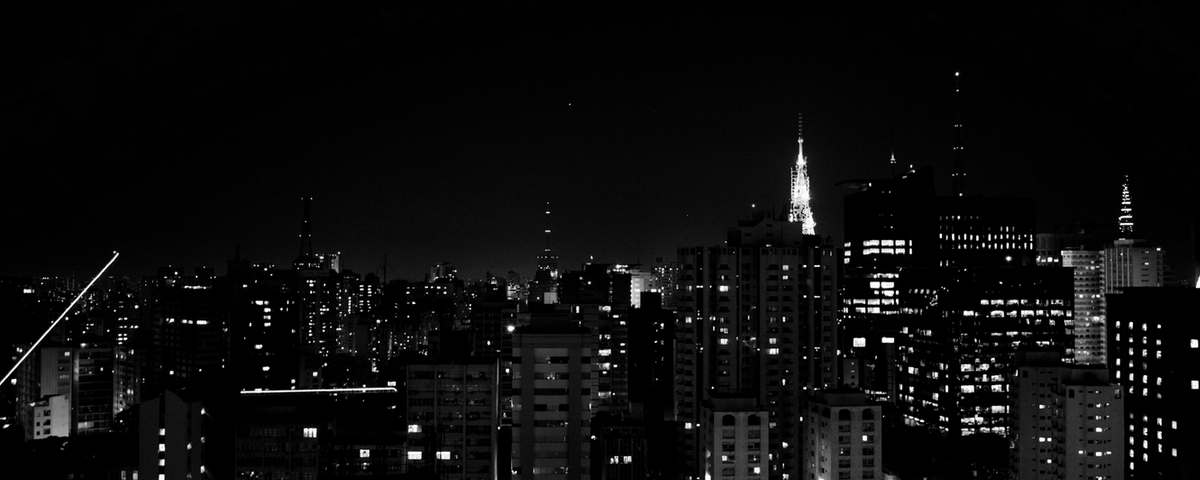 Foto em preto e branco de São Paulo durante a noite, com os prédios iluminados. 
