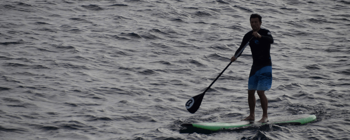 Homem praticando Stand Up Paddle no mar. 