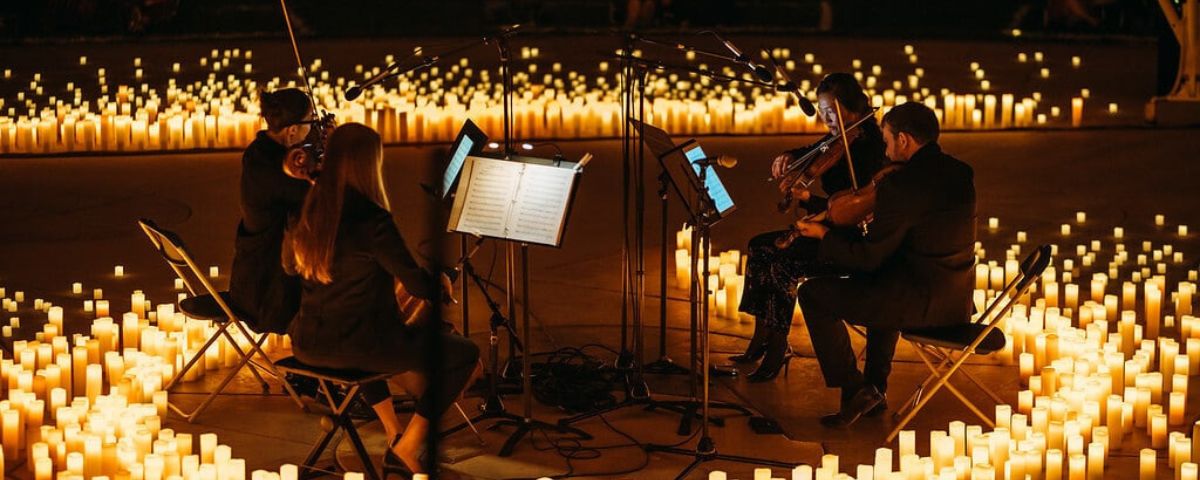 Músicos tocando instrumentos em meio a diversas velas no concerto Candlelight, um dos eventos em SP em fevereiro. 