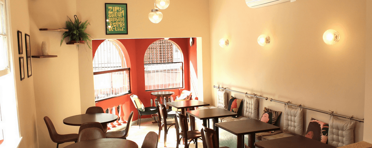 Salão do Tantin Bar possui mesas marrons e uma parede vermelha. 