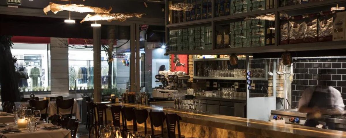 Salão do restaurante Il Capitale com banquetas no bar e mesas espalhadas. 
