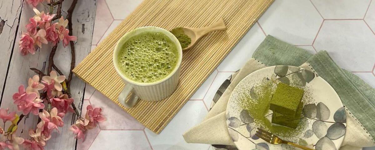 Mesa com chá verde servido em uma xícara e um doce verde também feito com o pó do chá. 
