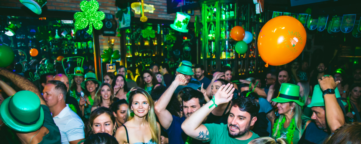 Diversas pessoas em pub, usando acessórios na cor verde em celebração ao St. Patrick's Day em São Paulo. 