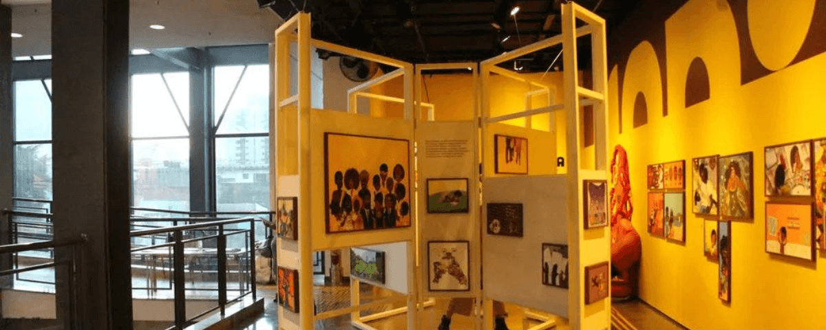 Mostruários com diversos quadros pendurados em uma exposição em Sampa. 