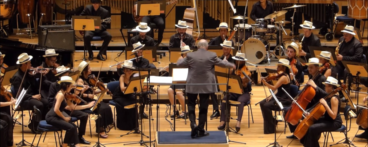 Orquestra tocando sendo regida por um maestro. 