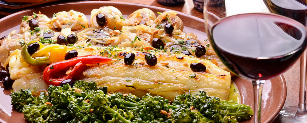 Bacalhau assado com brócolis, azeitonas e uma taça de vinho tinto. 