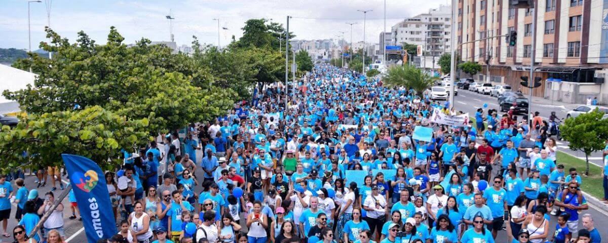 Diversas pessoas na rua, usando uma camiseta azul, enquanto participam da Caminhada pelo Autismo. 