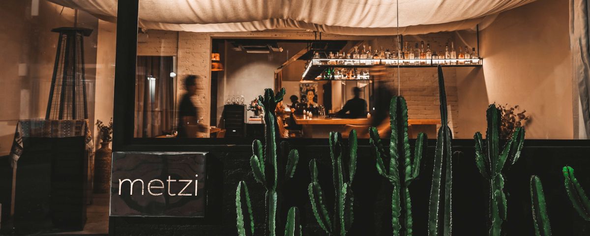 Outro entre os restaurantes charmosos em Pinheiros é o Metzi. Ele possui cactos na fachada e a luz dentro do restaurante é baixa, deixando o ambiente aconchegante. 