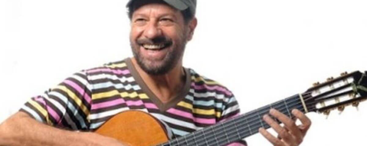 Cantor João Bosco segurando um violão e sorrindo. 