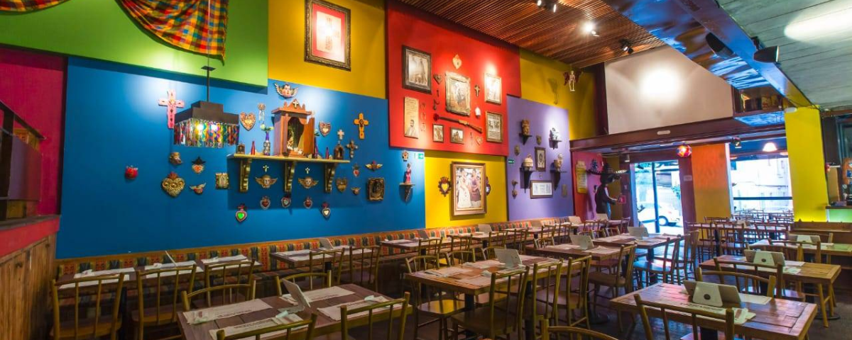 O salão do restaurante Mexicaníssimo tem paredes coloridas e objetos estilo mexicanos decorando o ambiente. 