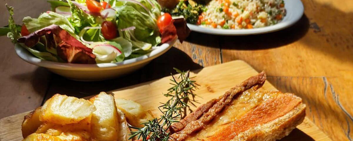 Mesa com salada e uma tábua com carne de porco, o menu faz parte do Dia das Mães em SP do Bar Brahma. 