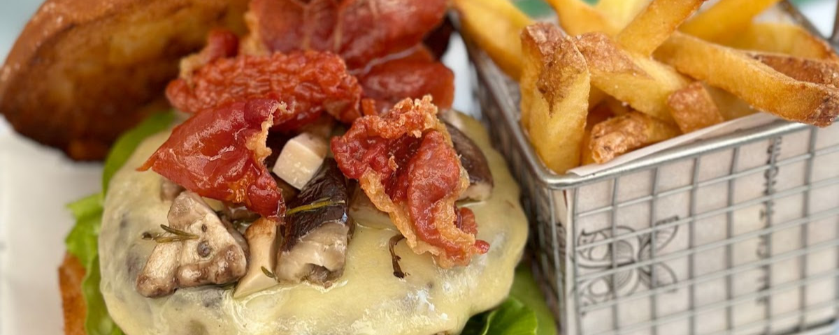 Hambúrguer com bastante bacon, cogumelos e queijo, e uma porção de batata frita ao lado. 