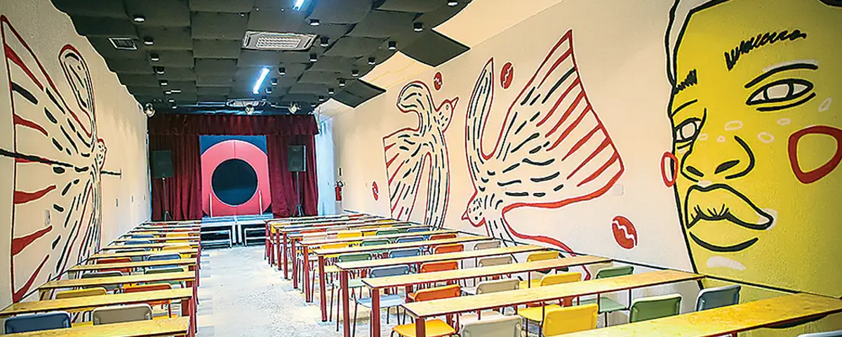Espaço do Boca Cultural possui diversas mesas e cadeiras e desenhos coloridos nas paredes. 