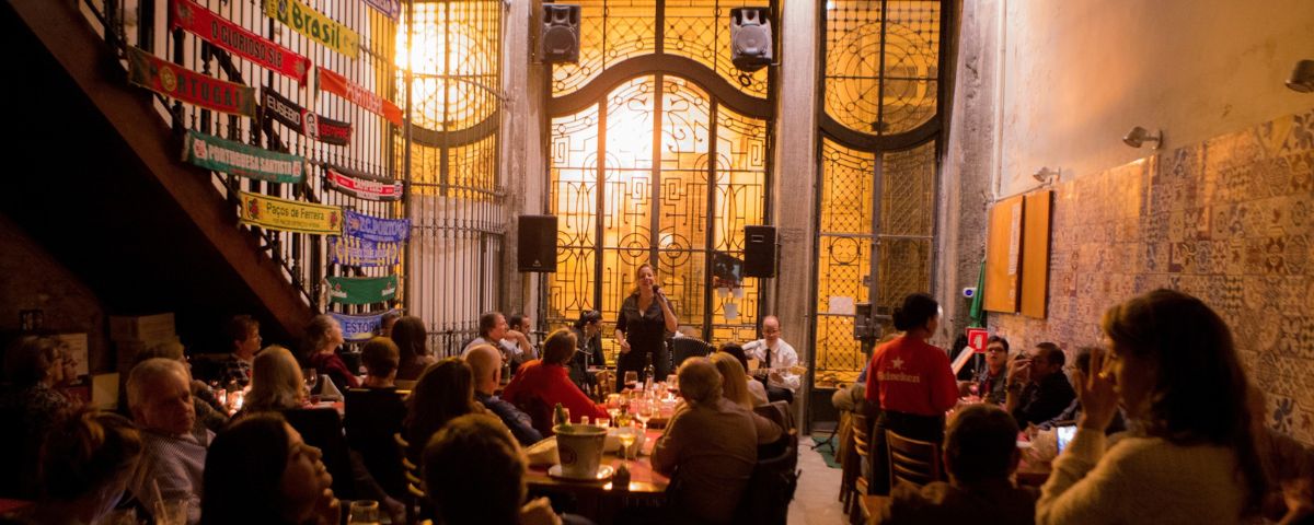 Salão do restaurante Tasca do Porto, com várias pessoas nas mesas e um vitral ao fundo. 