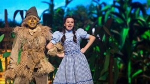 Dorothy e o homem espantalho estão caminhando sorridentes pela estrada de tijolos amarelos